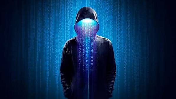 A mysterious hooded figure wearing a dark jacket, with cascading blue digital code and binary numbers overlaying the face and background, evoking a stereotypical hacker aesthetic.