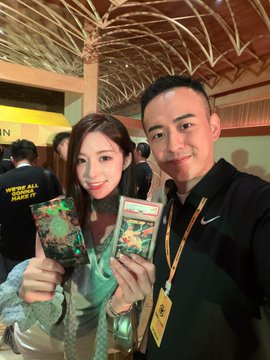 A smiling couple takes a selfie at a BNB Chain event, proudly showing off a Pokémon trading card, with the woman displaying a special Pikachu-themed card in a protective sleeve, matching the celebratory post about scoring the prized collectible at the event.