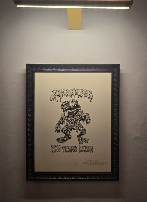 A framed black-and-white print hangs on a wall under a light, depicting a drippy 'Fear Street' logo above a sketch of a skeletal, monstrous creature and the text 'TEN YEARS LATER', along with what appears to be a signature and an edition number.