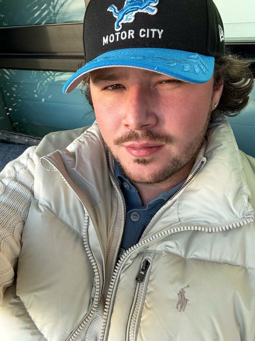 A selfie shows a man wearing a black and blue "MOTOR CITY" Detroit Lions cap and a cream-colored Polo Ralph Lauren puffer vest, paired with a post celebrating "GM" (good morning) on a happy Thursday.