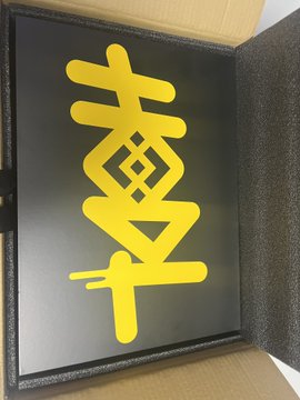 A glowing yellow symbol resembling a stylized Chinese character or sigil (possibly related to Mamacoins/Mothercoin cryptocurrency) displayed on a black sign or screen.