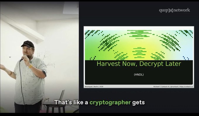 A man wearing a cap speaks into a microphone alongside a presentation slide titled 'Harvest Now, Decrypt Later (HNDL)' by Richard S. Carback at the qup network, with subtitles reading 'That's like a cryptographer gets'.