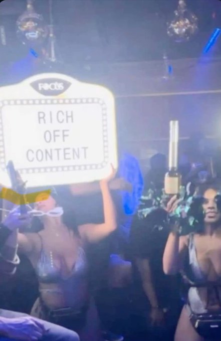 A nightclub scene with women holding a sign reading 'Finchs RICH OFF CONTENT' and a bottle of champagne amid blue lighting and disco balls.