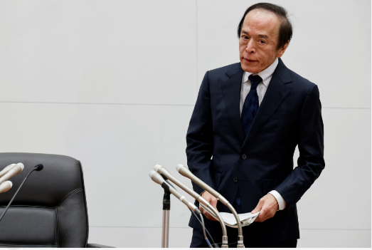 An elderly Japanese man in a dark suit and tie stands at a podium with multiple microphones, appearing to address an audience in a formal setting. The image likely depicts BOJ Governor Kazuo Ueda during a policy announcement, contextualizing the post about the Bank of Japan's rate hike to 1.25%—the highest in 31 years—amid coordinated tightening by major central banks.