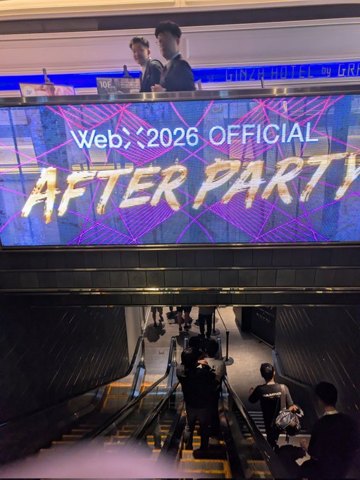 People ride down an escalator beneath a large illuminated sign that reads "WebX 2026 OFFICIAL AFTER PARTY," advertising the official afterparty event for the WebX 2026 conference.
