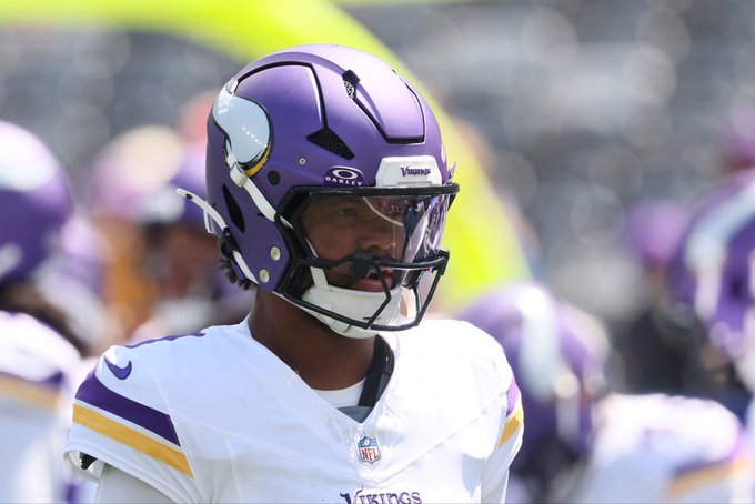 A football player wearing a purple Minnesota Vikings helmet with an Oakley visor stands on the field in a white jersey with purple and yellow trim.