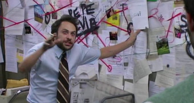 The image features a man wearing glasses with a beard standing next to a wall covered in various notes and papers. He seems engrossed in an activity or discussion. There are also some documents, including one that says "we love", possibly signifying his interests or goals. Another person is partially visible on the left side of the image but does not appear to be interacting with the man. The overall atmosphere suggests a casual and social setting where people might gather for discussions or share ideas.
