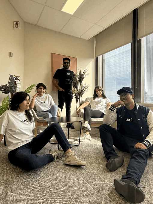 Five team members wearing ".sol" branded shirts and jackets pose casually together in a modern office lounge, with one person standing behind a framed ".sol" wall display. The relaxed group setting reflects the post's sentiment about the community spirit of those building on Solana, showing the collaborative "people" aspect behind the project.