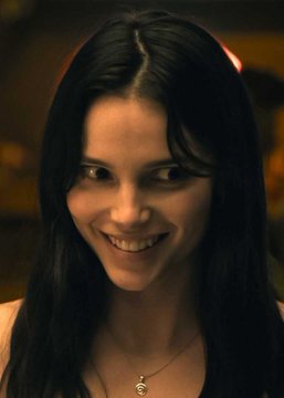 A woman with long dark hair smiles warmly while wearing a delicate gold necklace, her expression conveying a confident charm that complements her status as a 2nd favorite contender for Best Actress at the Oscars. The intimate, softly-lit portrait captures a moment of poised anticipation fitting for the "Obsession" leading lady ranked just behind Julianne Moore by Polymarket US bettors.