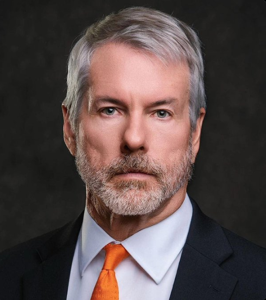 A portrait of a serious-looking older man with gray hair and beard, wearing a black suit and bright orange tie, likely representing an executive making the case for a Bitcoin treasury sell-off and stock buyback. The polished corporate headshot pairs with the post's tone of confident financial commentary, visually anchoring the "WHALE WATCH" argument with the image of a seasoned business leader.