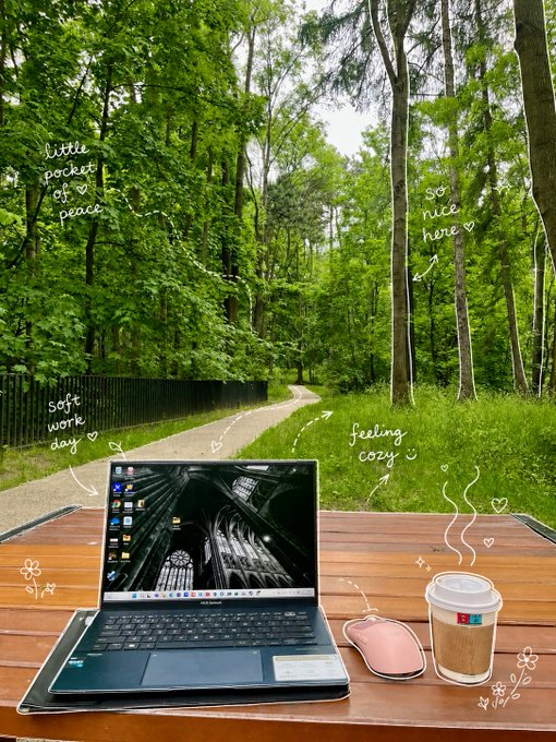 A scenic park photo with a laptop, coffee cup, and mouse on a wooden table in the foreground, decorated with hand-drawn text annotations like 'little pocket of peace,' 'so nice here,' 'soft work day,' and 'feeling cozy.'