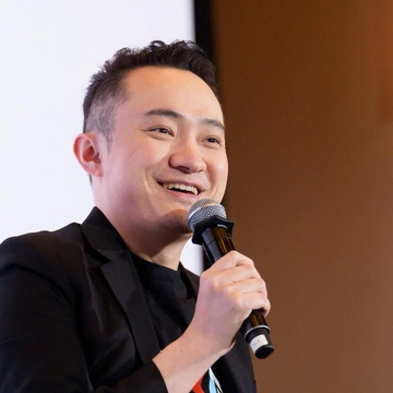 Justin Sun, founder of Tron, smiles while speaking into a microphone at what appears to be a public event or conference. The image accompanies news about a California court ruling in his favor regarding his legal dispute with World Liberty Financial.