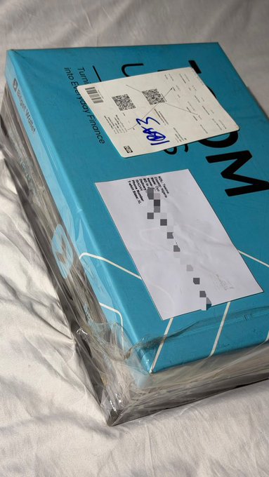 Two blue packages from BitGet, wrapped in plastic and labeled with "Turn your information into your finances," sit on a white sheet, containing an undisclosed Bitget merchandise delivery for the user.