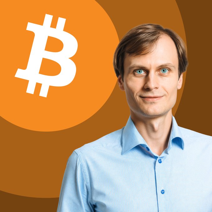 A portrait of a man in a light blue shirt next to a large white Bitcoin symbol on an orange circular background.