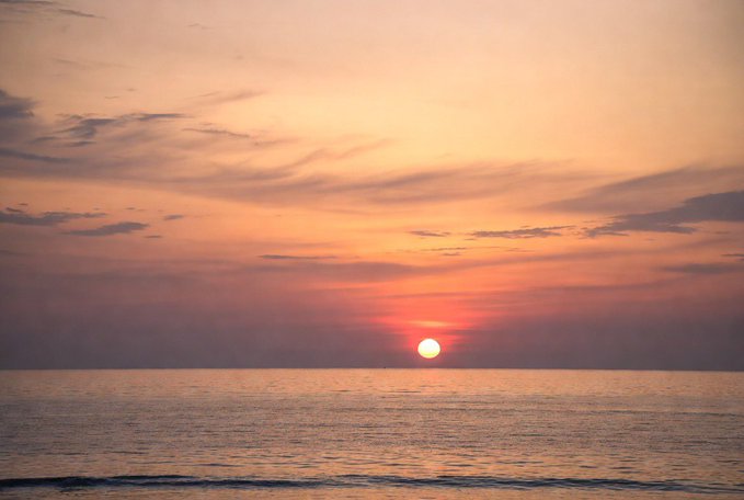 A serene sunset over the ocean, with the sun low on the horizon and orange and purple hues in the sky.