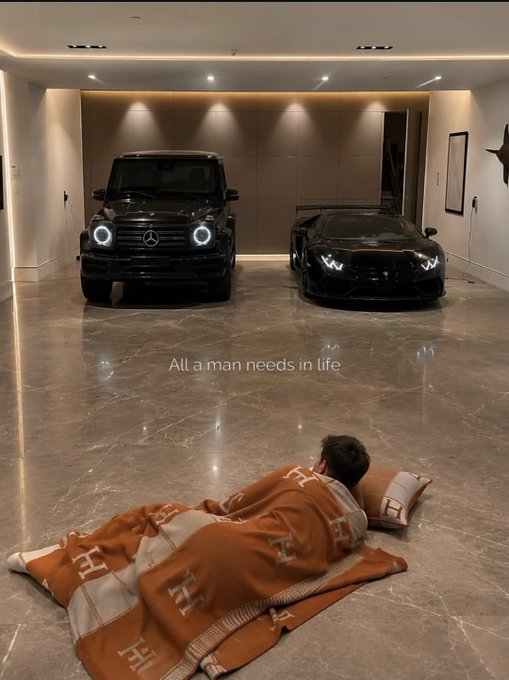 A humorous photograph shows a person lying on a Hermès blanket on the floor of a luxury garage, facing two parked black vehicles (a Mercedes G-Wagon and a Lamborghini) with the caption 'All a man needs in life' displayed on screen.