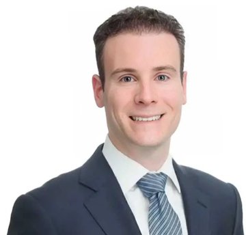 A professional headshot of a smiling man in a dark suit and striped blue tie against a white background.