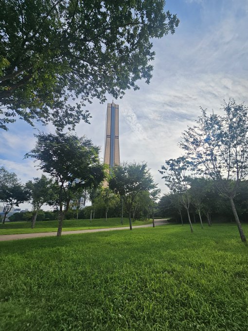 A tall monument rises above a lush green park with scattered trees and a winding path under a partly cloudy sky, though no text or numbers are visible in the image. The accompanying post references an XRP cryptocurrency prediction to $589 with #XRP hashtags, but the serene park scene bears no connection to the crypto post beyond being a mismatched upload.