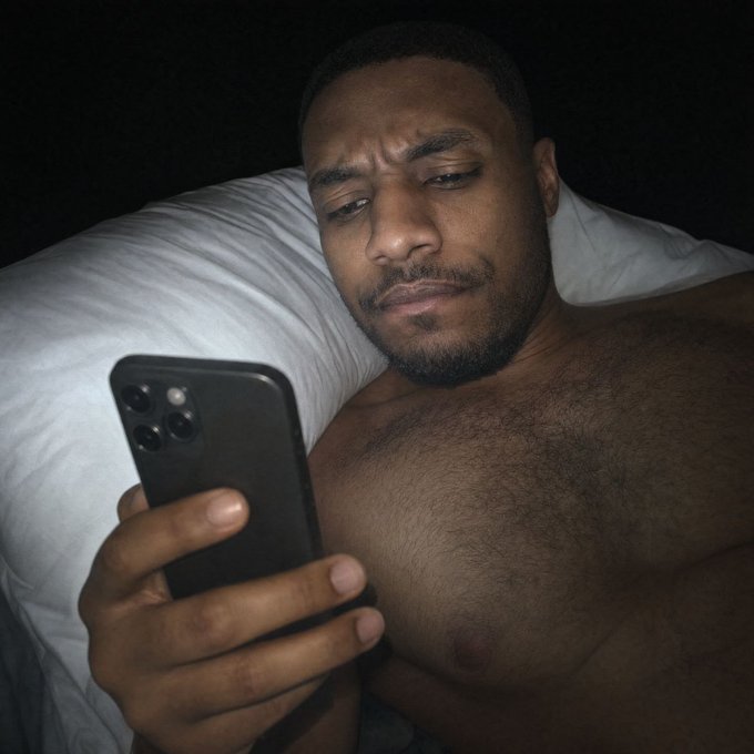 A shirtless man lies in bed with a concerned, squinting expression while looking at his smartphone, capturing the relatable "GM" crypto community ritual of anxiously checking their phone for $ANSEM updates first thing in the morning.