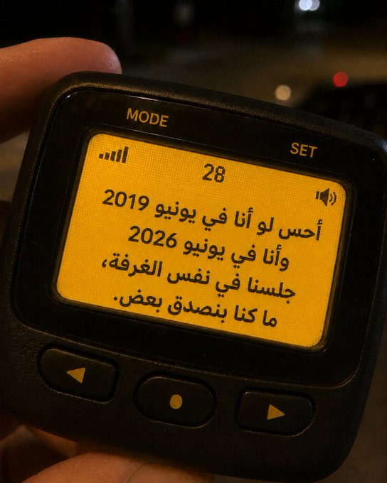 A hand holds a small black digital device displaying an Arabic reflection: "I felt lost in June 2019 and again in June 2026, sitting in the same room, but we heal by believing." The image visually echoes the post's message about growth, capturing a moment of personal reflection across seven years in the same place.