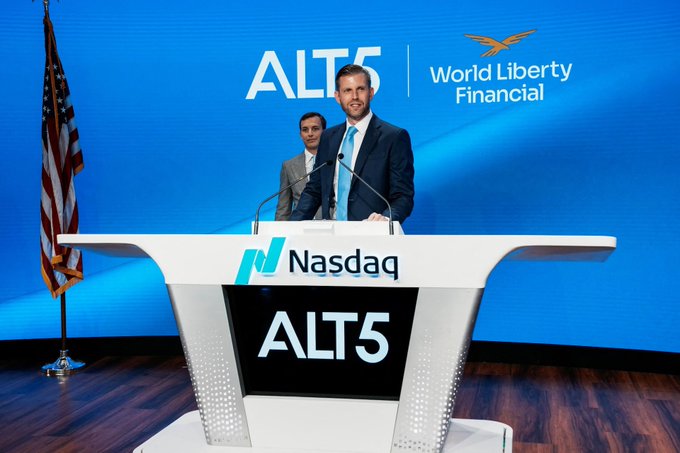 Two men stand at a Nasdaq podium during an event for ALT5, with a screen and backdrop displaying the 'ALT5' and 'World Liberty Financial' logos alongside an American flag.