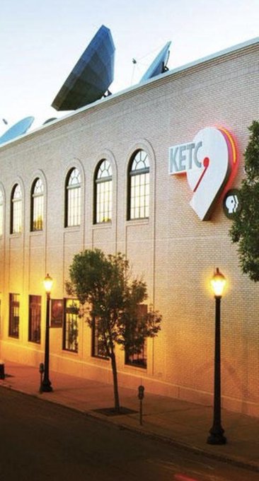 The image shows the exterior of a KETC 9 building, a public television station, with large satellite dishes mounted on its roof and a prominent illuminated "KETC 9" logo on the brick facade. The caption can be: "Outside the KETC 9 broadcasting station, where satellite dishes signal the reach of public television—turning a brief mention into a real-world learning moment."