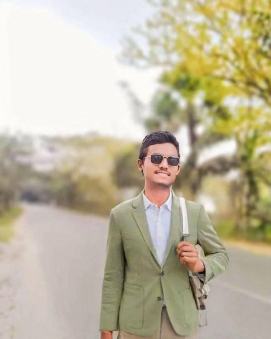 A man wearing sunglasses and a light green blazer stands on a road carrying a bag, rendered with a tilt-shift effect.