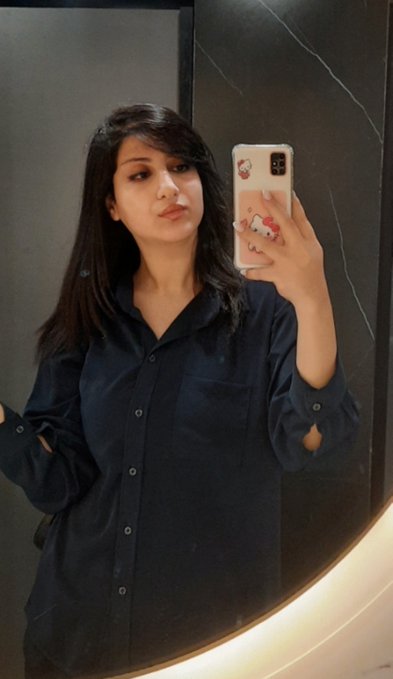 A young woman with long dark hair takes a mirror selfie wearing an oversized dark navy button-up shirt, holding a phone with a Hello Kitty character case. The casual, low-key aesthetic of the photo complements the "GN𐙚" (good night) caption, suggesting a relaxed nighttime moment.