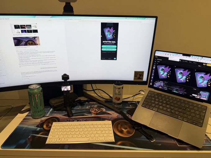 A desk setup featuring a curved monitor and laptop displaying Discord and a browser, with a Monster energy drink, a small camera, and a space-themed desk mat.