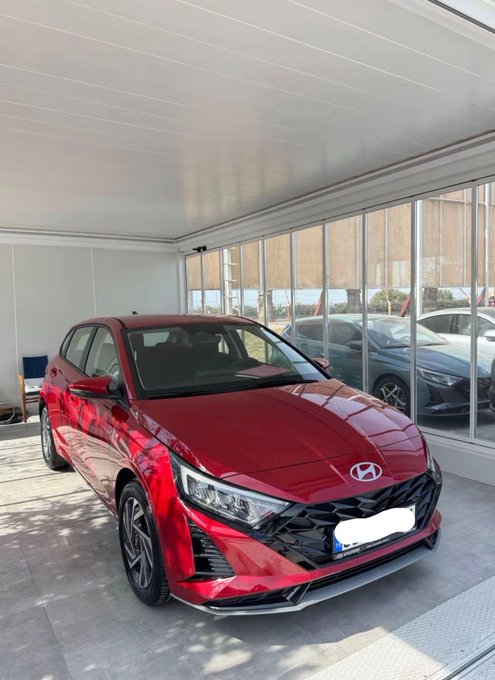 A shiny red Hyundai hatchback is parked under a covered showroom structure.