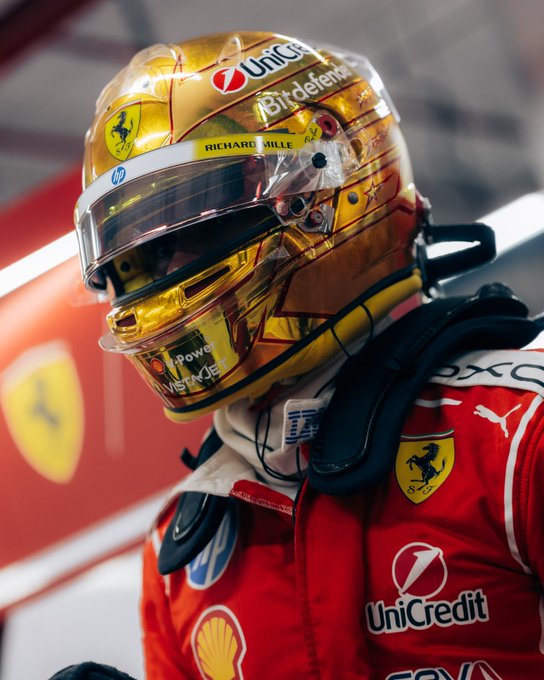 A Ferrari driver wearing a gold-hued helmet sponsored by UniCredit and Richard Mille, alongside Puma, Shell, and HP logos on his racing suit, stands in the garage following a successful Sprint weekend that delivered a double podium for Scuderia Ferrari.