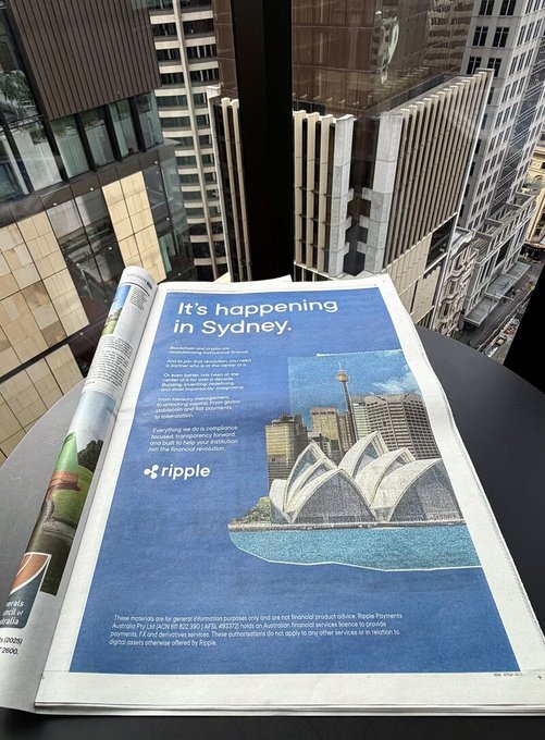 The image features an open newspaper with an advertisement for Ripple, a cryptocurrency company, displayed prominently on its cover. The text of the advertisement reads "It's happening in Sydney," indicating that Ripple is promoting their services or products related to cryptocurrencies in Australia. The advertisement also mentions that Ripple has just bought a full-page ad in the Australian Financial Review, which suggests that the company is actively engaging with financial news and events in the country. This highlights how cryptocurrency companies are leveraging traditional media platforms like newspapers to reach potential customers and investors interested in the crypto space.