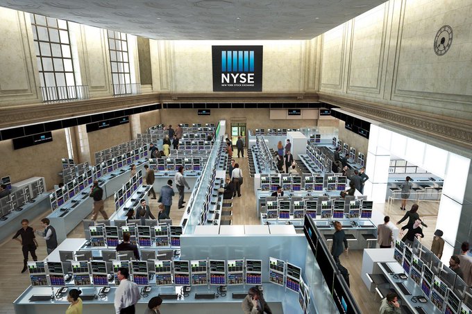 An aerial view of a busy trading floor with rows of monitors and traders, with a logo on the wall reading 'NYSE NEW YORK STOCK EXCHANGE'.