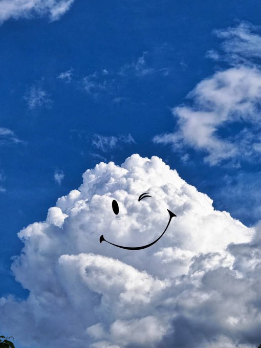 A fluffy white cloud against a bright blue sky has been digitally edited to display a cheerful winking smiley face, perfectly matching the upbeat "good morning" greeting and well-wishes for a beautiful day.