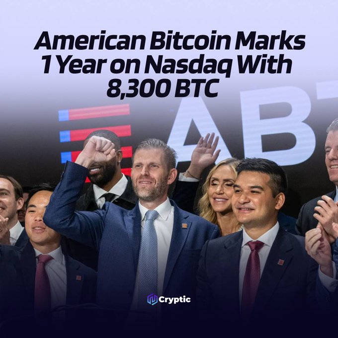 A group of people celebrate on stage with raised fists and smiles in front of a screen displaying "ABT," accompanied by the headline "American Bitcoin Marks 1 Year on Nasdaq With 8,300 BTC," and the Cryptic logo at the bottom.