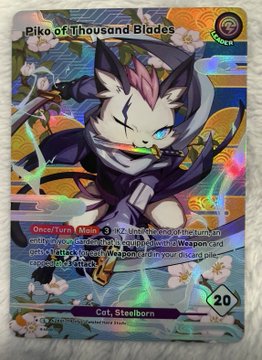 The image features a card with a cat as its main subject, surrounded by flowers and other elements that create an artistic and visually appealing scene. The card has a unique design, possibly resembling a Pokémon or anime character, which adds to its visual appeal. The text on the card reads "Biko of Thousand Blades" and "Cot. Steelborn", indicating the creator's name and the type of character they have designed for the card.