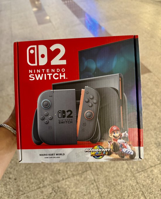 A photo of a Nintendo Switch 2 console box bundled with Mario Kart World, held by a person on a tiled floor.