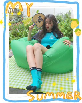 The image features a woman sitting on an inflatable chair, holding a fan or air mattress with her legs crossed while wearing blue socks. The background of the photo includes a green and white checkered blanket, which adds to the summery atmosphere. The caption "My Summer" suggests that this scene is part of a larger collection or series related to the theme of summertime activities or relaxation.