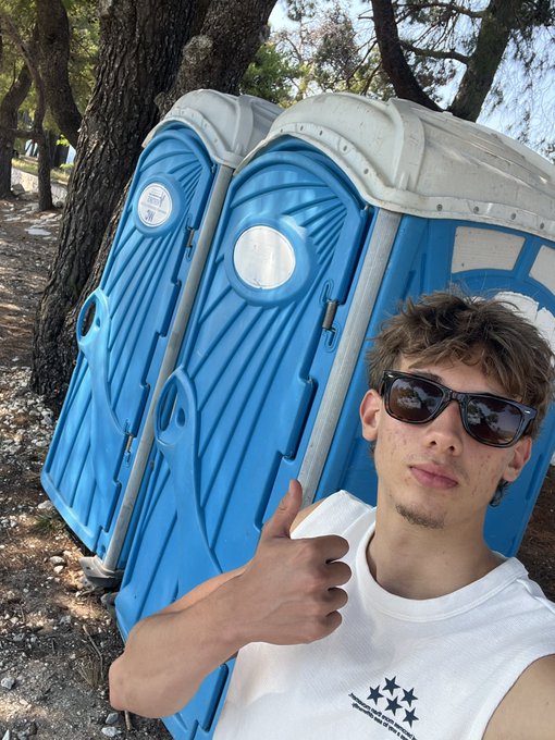 A young man wearing dark sunglasses and a white t-shirt with three star logos gives a thumbs-up while posing in front of two blue portable toilets set among trees, humorously framing them as "Bitcoin and Ethereum" chatting with him. The post jokes that the porta-potties gave bullish crypto advice, with the graffiti "ATH" (all-time high) visible on one of the units reinforcing the tongue-in-cheek bullish sentiment.