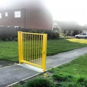 A bright yellow metal gate installed on a concrete pathway in front of a brick house with green lawn.