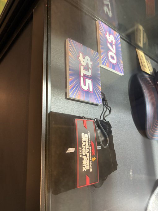 A black wristband from the Singapore Grand Prix 2024 sits on a glass surface alongside colorful price tags displaying '$25' and '$70'.