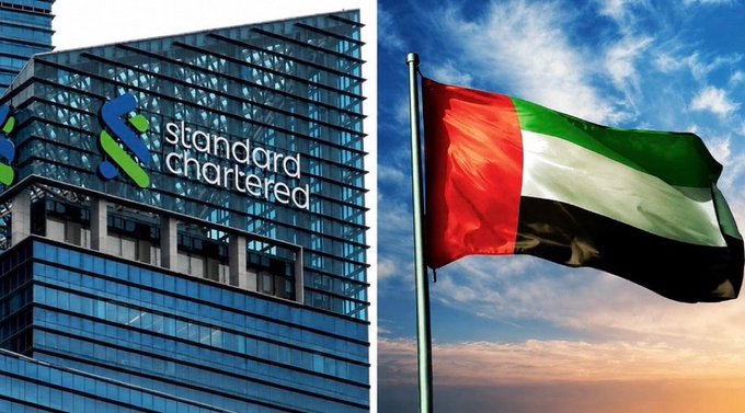 The image is split between a Standard Chartered bank building on the left, displaying its logo and name on the glass facade, and the United Arab Emirates flag waving on the right against a sunset sky. The visual pairing directly illustrates the news of Standard Chartered expanding its crypto trading services to wealthy clients in the UAE.