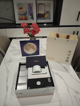 A marble table displaying an elegant gift set that includes a card featuring an image of the moon, a small decorative object, and a paper bag with Chinese characters that read '月下名物.'