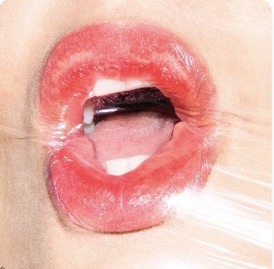 Extreme close-up photograph of red lips parted open, showing teeth and tongue, with a bright lens flare across the image.