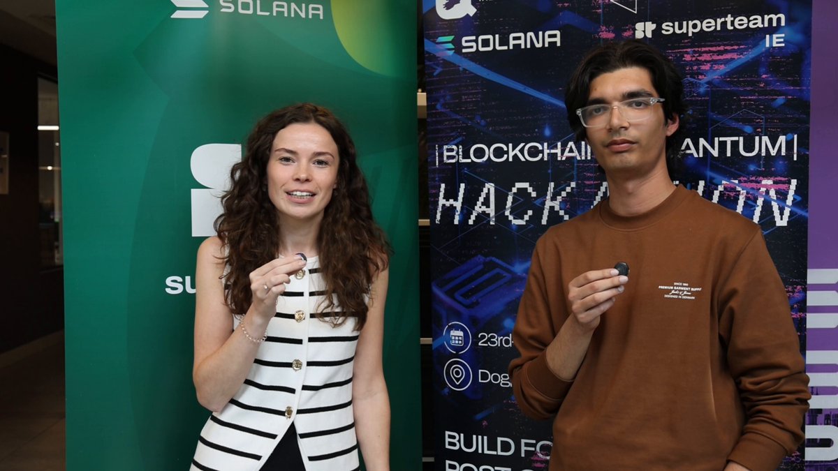 The image features a man and woman standing next to each other, both holding up electronic devices such as cell phones or tablets. They are positioned against a green backdrop with white text that reads "Q-Day is approaching. Prepare & Listen to our Quantum Hackathon winner @jaypopat0 @solana @FCATalyst". The people in the image appear to be posing for a photo, possibly at an event related to technology and innovation.