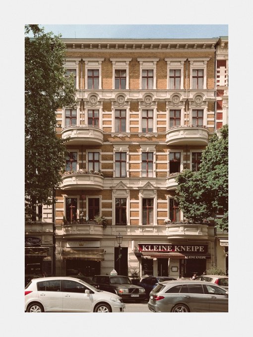 A multi-story brick and stone apartment building with ornate balconies and a ground-floor 'KLEINE KNEIPE' restaurant.