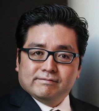 A professional headshot of an East Asian man wearing glasses and a dark suit against a dark background.