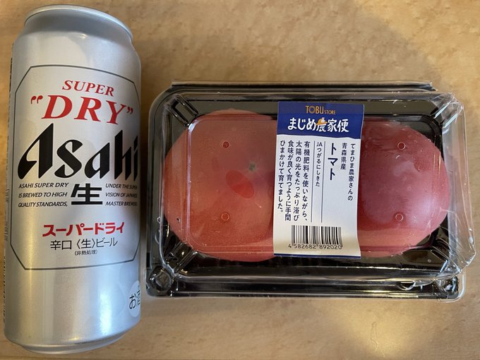 A can of 'SUPER "DRY" Asahi' beer next to a plastic package containing two pink Japanese tomatoes labeled 'まじめ農家便 トマト' from Tobu-Tore.