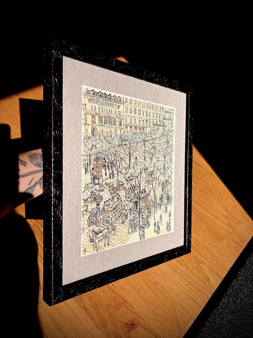 A framed print depicting a bustling Parisian street scene with trams and pedestrians rests on a wooden surface, waiting to be hung. The caption references the wife's approving verdict and hints at the artwork's significance as a new addition to their walls, aligning with their enthusiasm for the degen poet and $TOADS.