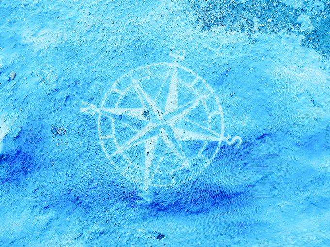 A blue textured wall featuring a white spray-painted pentagram or star symbol, with the letter 'S' visible next to it.